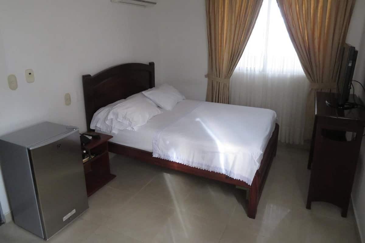 A hotel room with a bed, a desk, a chair, a TV, and a refrigerator.
