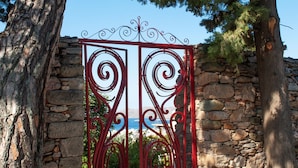 A stone wall with a red metal gate, trees, and a clear sky.