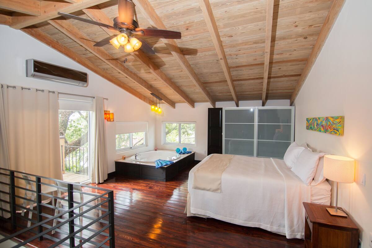 A bedroom with a large bed, a bathtub, and a balcony with a view.