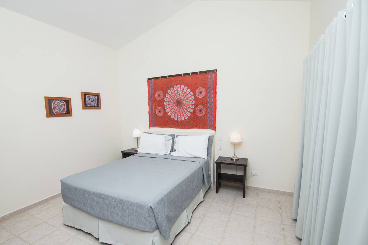 A neatly arranged bedroom with a bed, two bedside tables, a red tapestry, and two framed pictures on the wall.