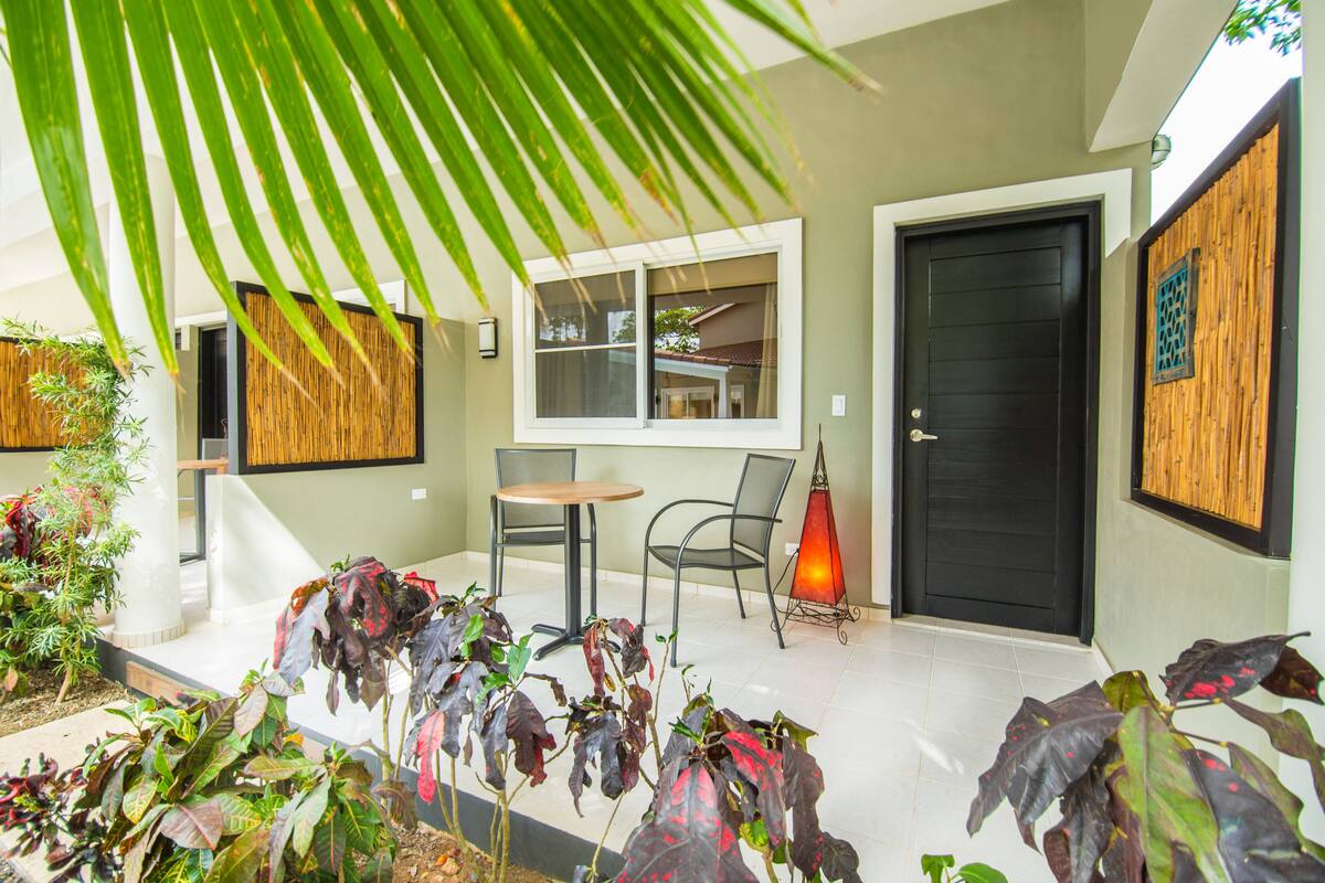 A modern outdoor seating area with a table and chairs, surrounded by plants and a decorative wall.