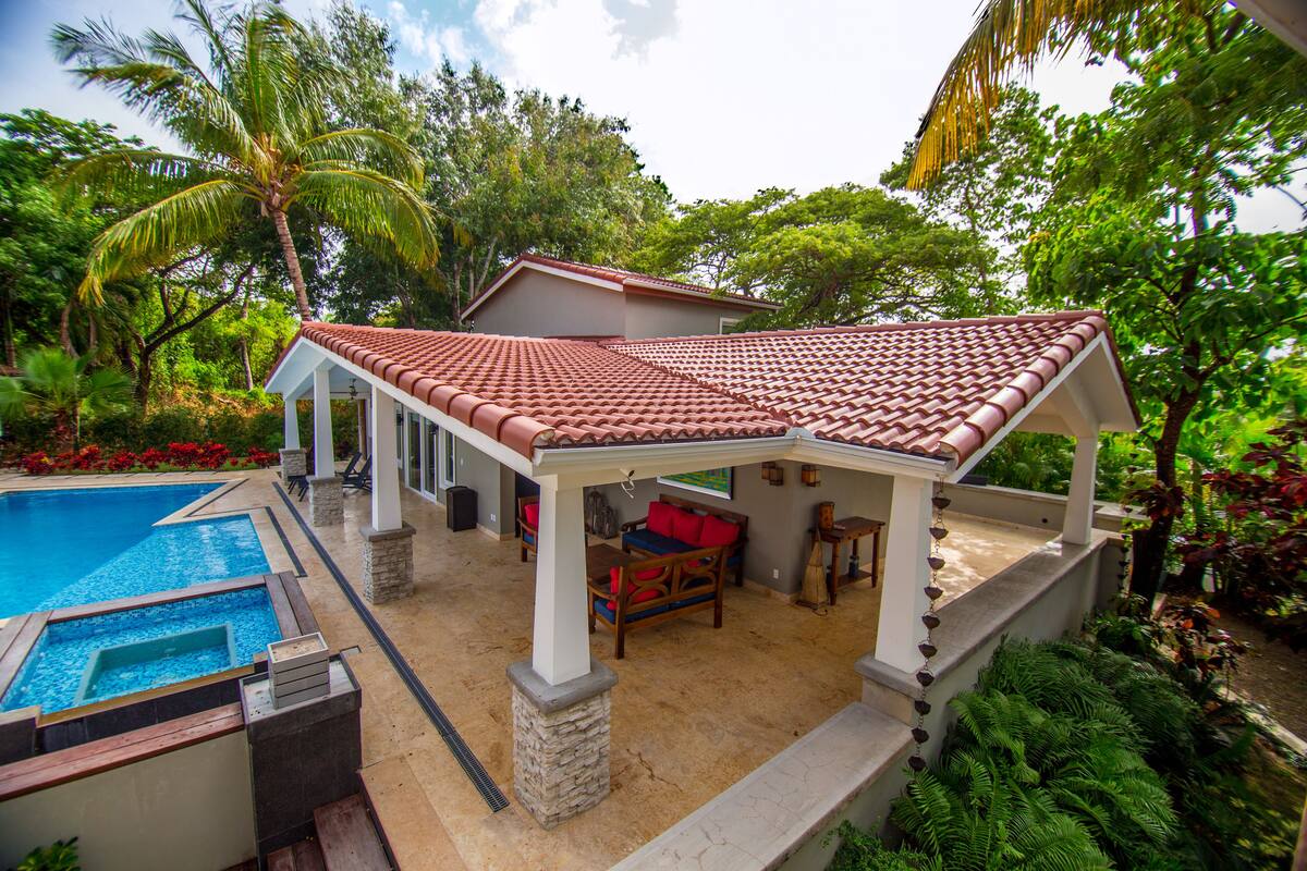 A covered outdoor area with a pool, seating, and lush greenery.