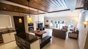 Cozinha moderna com uma ilha central, área de jantar com mesa e cadeiras, sofá e televisão.