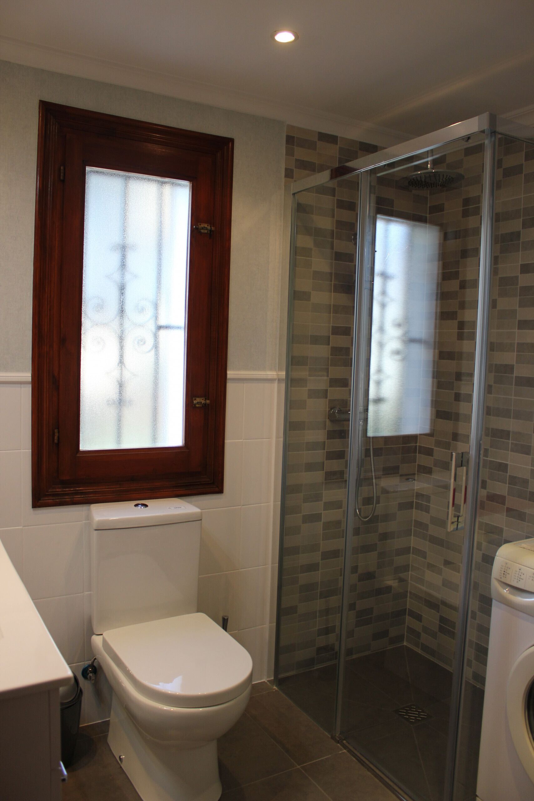 Ein Badezimmer mit Toilette, einer Duschkabine und einem Fenster mit Milchglas.
