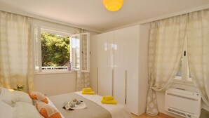A bedroom with a bed, a wardrobe, a window with curtains, and an air conditioning unit. - Beachfront Apartment Barbara, near Bacvice beach walking distance from old town  (Split)
