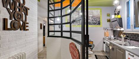 A modern kitchen with a white brick wall, a 'DO WHAT YOU LOVE' sign, a 'BISTRO' sign, and a view of the street through a glass partition.