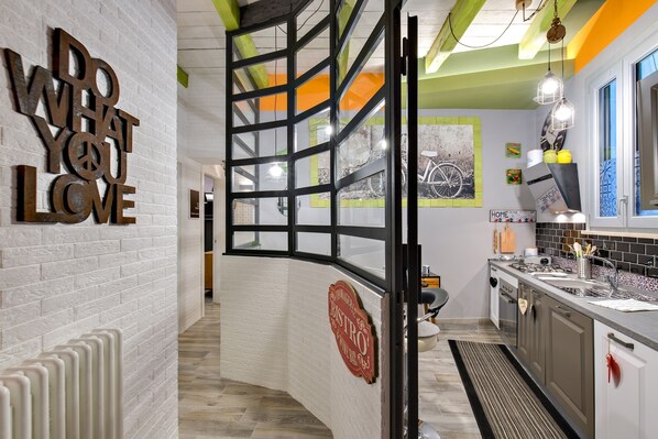 A modern kitchen with a white brick wall, a 'DO WHAT YOU LOVE' sign, a 'BISTRO' sign, and a view of the street through a glass partition.