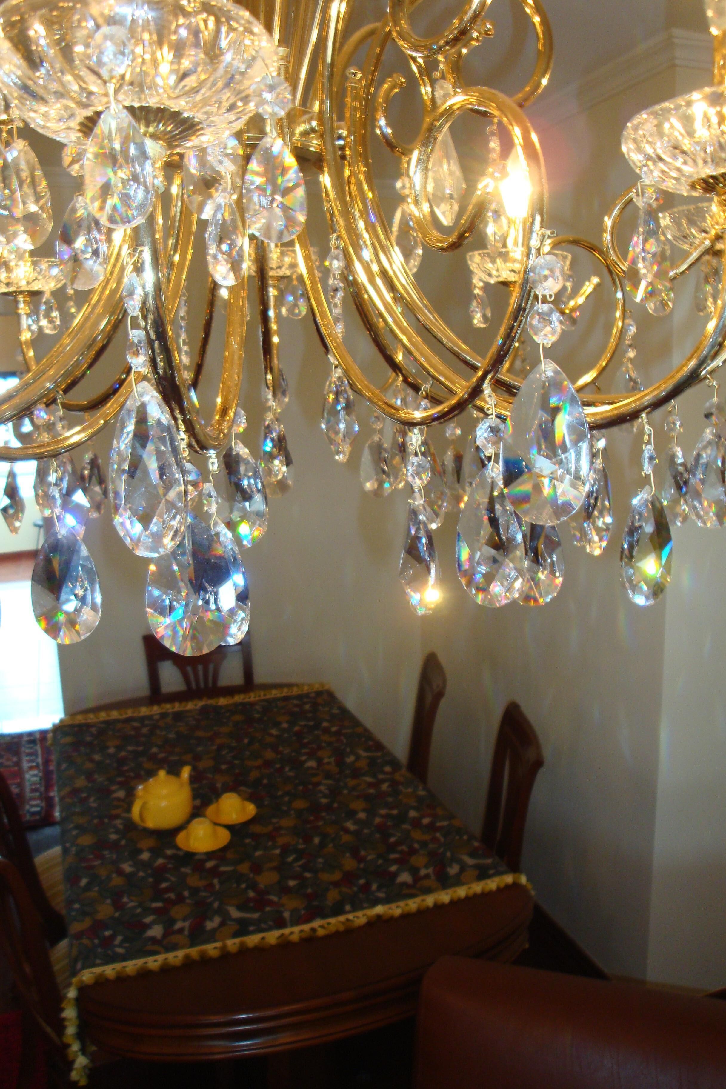 A chandelier with multiple crystal elements and a table with a patterned tablecloth and yellow teapots.