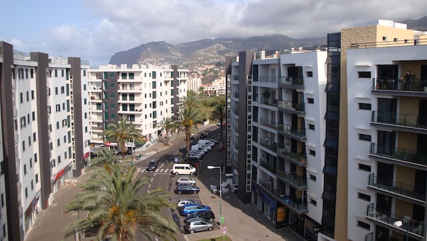 A high-rise residential building with multiple balconies, a parking area with cars, and a street lined with palm trees. - Funchal beach area - Sea view - Free Wifi (Funchal)