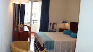A hotel room with a bed, a chair, a desk, a lamp, and a window with curtains. - Funchal beach area - Sea view - Free Wifi (Funchal)