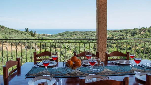 A table set for two with a view of the sea, a wooden table, metal chairs, and a glass bowl with bread. - Peaceful and private family villa, big pool, wellness, views of sea and mountain (Chania Crete)