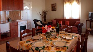 A dining area with a table set for four, surrounded by wooden chairs. There is a sofa and a television in the background. - Peaceful and private family villa, big pool, wellness, views of sea and mountain (Chania Crete)