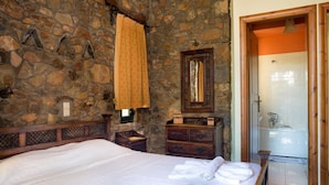 A stone-walled bedroom with a bed, wooden dresser, and a bathroom with a bathtub. - Amazing Sea View villa w/pool, close to Elafonissi (Livadia)