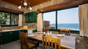 A dining area with a table set for two, a stone wall, and a view of the ocean. - Amazing Sea View villa w/pool, close to Elafonissi (Livadia)