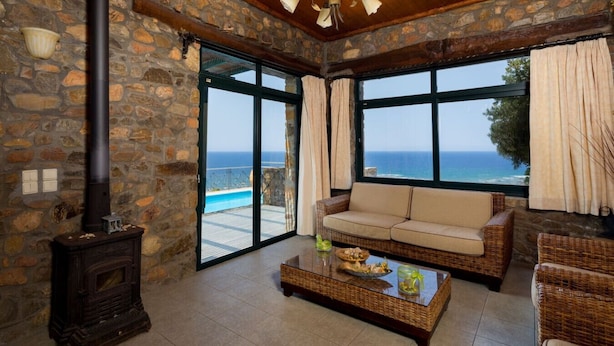 A stone-walled room with a fireplace, a sofa, a coffee table, and a large window overlooking the sea. - Amazing Sea View villa w/pool, close to Elafonissi (Livadia)