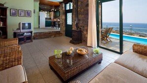 A living room with wicker furniture, a glass coffee table, a television, and a view of the ocean. - Amazing Sea View villa w/pool, close to Elafonissi (Livadia)