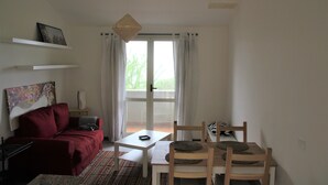 A room with a red sofa, a small table, a wooden chair, and a view through a glass door.