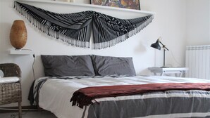 A bedroom with a bed, a desk, a chair, a hanging tapestry, and a radiator.