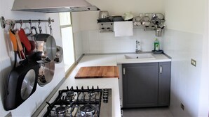 A kitchen with a gas stove, hanging pots, a wooden cutting board, and a sink.