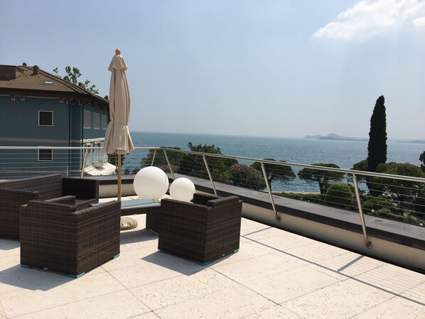 Una terraza en la azotea con mobiliario de mimbre, una sombrilla y vistas al mar.