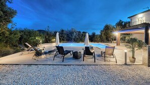 A poolside area with lounge chairs, umbrellas, and a well-lit pool at dusk. - Luxury villa with heated pool, Marina-Trogir (Pozorac, Marina)