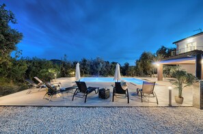 A poolside area with lounge chairs, umbrellas, and a well-lit pool at dusk. - Luxury villa with heated pool, Marina-Trogir (Pozorac, Marina)