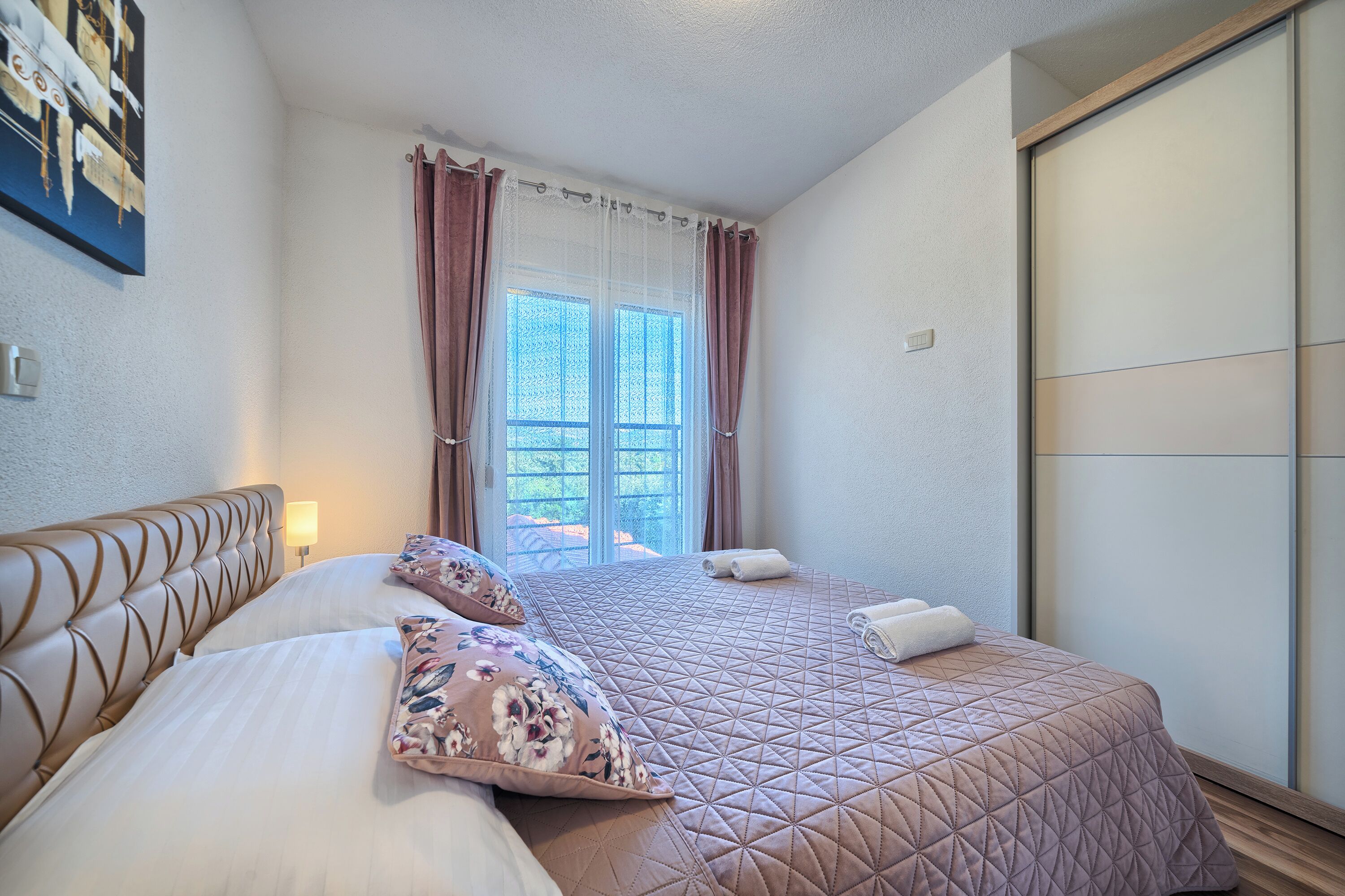 A hotel room with a bed, a nightstand, a window with curtains, and a sliding door.