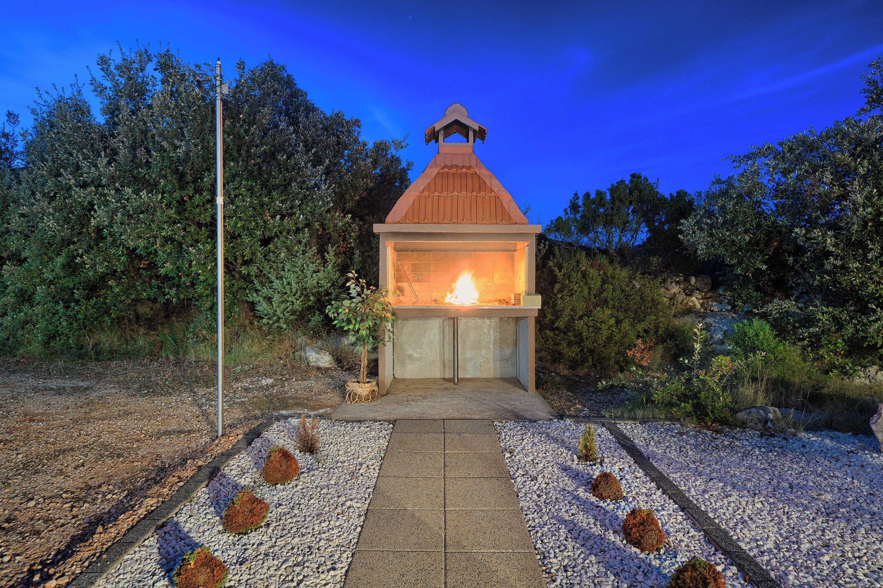 A small outdoor structure with a fire, surrounded by gravel and plants.