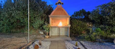 A small outdoor structure with a fire, surrounded by gravel and plants.