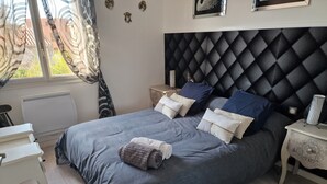 Un dormitorio con una cama grande, una mesita de noche, un radiador y una ventana con cortinas.