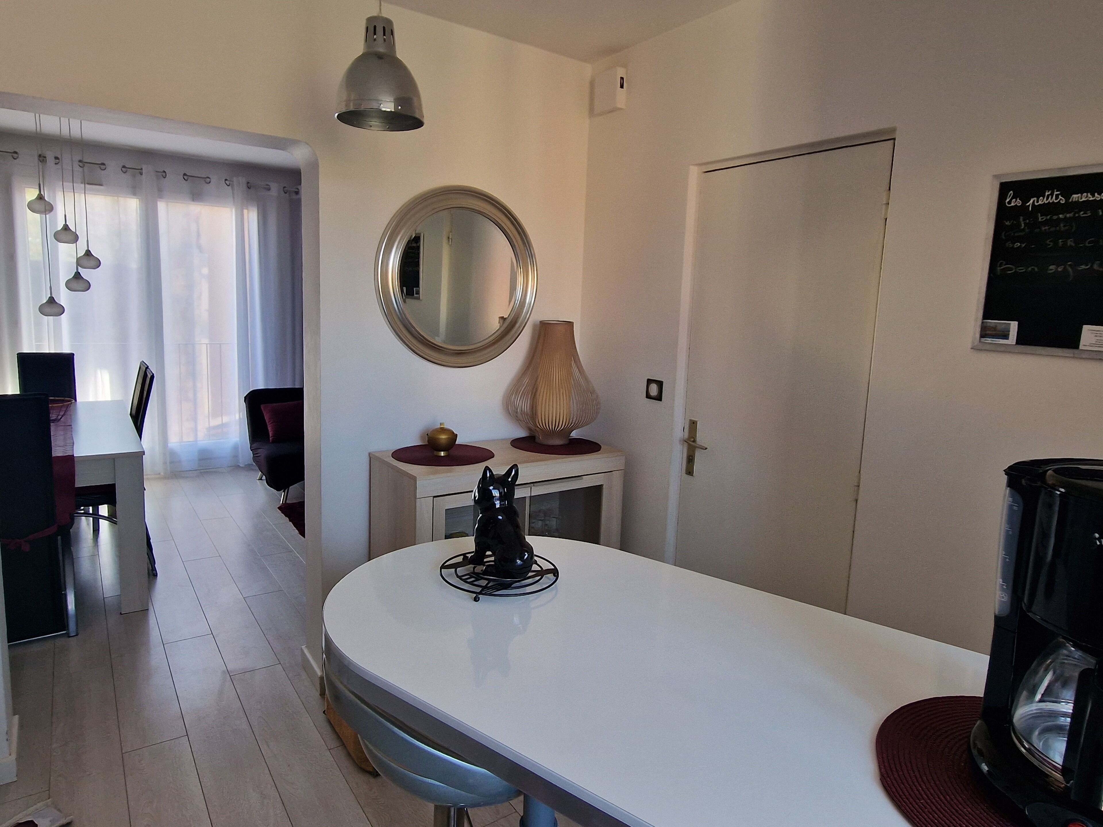 A modern kitchen with a white countertop, a round mirror, and a coffee maker.