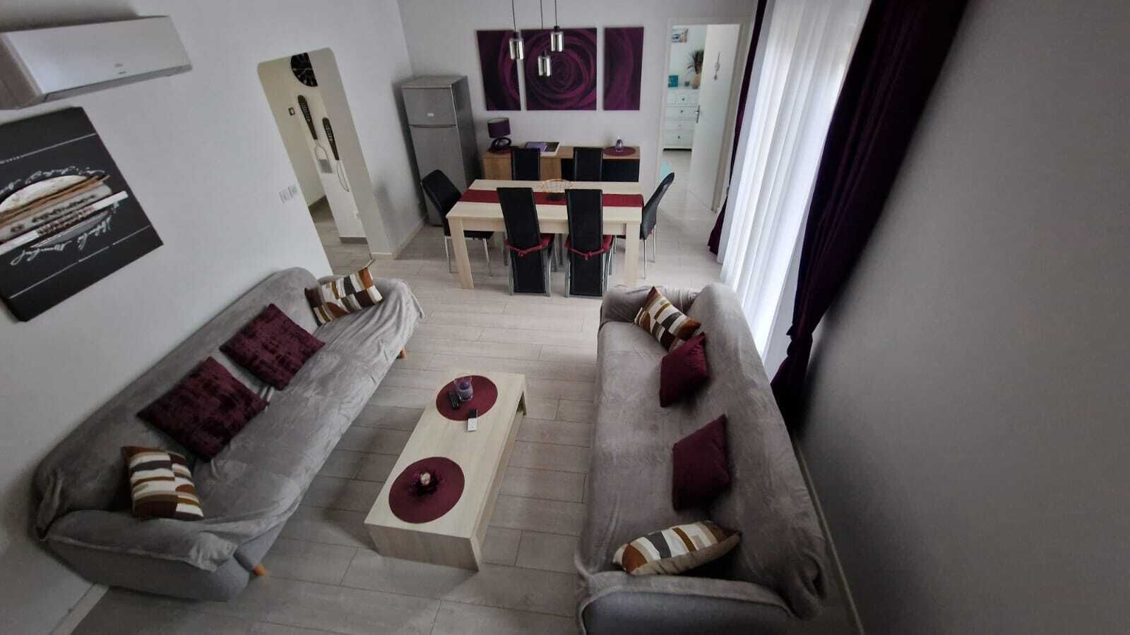 A modern living room with a grey sofa, a coffee table, and a dining area with a table and chairs.