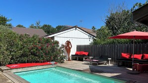 En trädgård med en pool, ett trädäck och en utomhusplats med sittmöbler och röda kuddar.