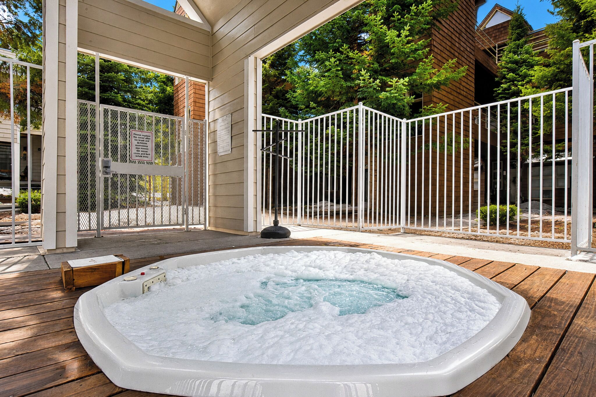A hot tub on a wooden deck with a white fence and a wooden house in the background.