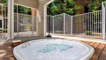 A hot tub on a wooden deck with a white fence and a wooden house in the background.