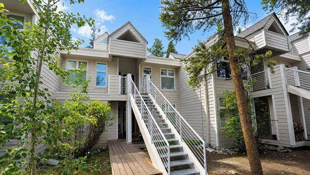 A multi-story residential building with a central staircase, a deck, and a surrounding wooded area. - River Glen Streamside Condo: Stroll To Main St, Shuttle Stop (Frisco)