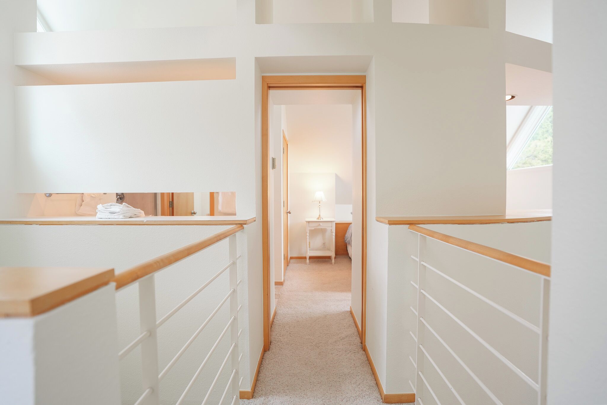 A narrow hallway with wooden railings, leading to a bedroom with a bed and a nightstand.