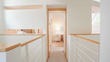 A narrow hallway with wooden railings, leading to a bedroom with a bed and a nightstand.