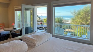 A bedroom with a large window offering a view of the ocean and a balcony with outdoor seating. - Captain's House ~ amazing ocean view, 2 min walk to beach, near Cannon Beach (Arch Cape)