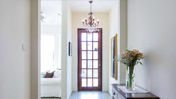 Un couloir avec une porte en bois, un lustre, un vase rempli de fleurs et une petite table.