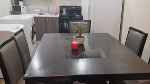 Une cuisine compacte avec des meubles blancs, une cuisinière noire et un four à micro-ondes. Une table à manger avec des chaises se trouve au premier plan.