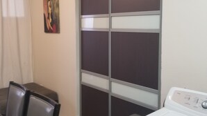 Une pièce comprenant une table à manger et des chaises, une grande porte coulissante avec des panneaux en verre dépoli, un lave-linge et un appareil de climatisation fixé au mur.