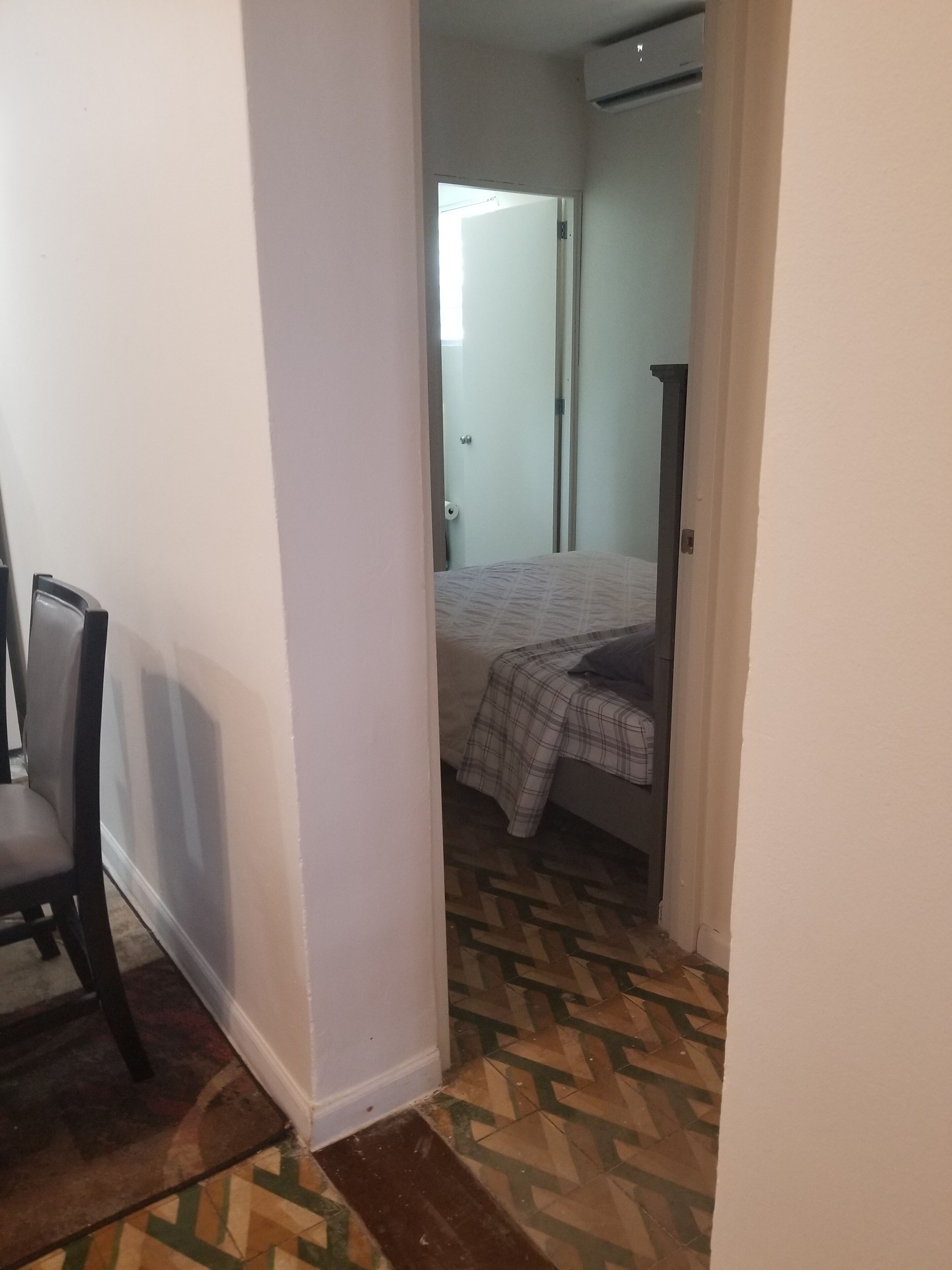 Un couloir étroit mène à une chambre à coucher qui contient un lit et une chaise. La pièce est dotée d’un sol carrelé et d’une porte qui donne sur une autre pièce.