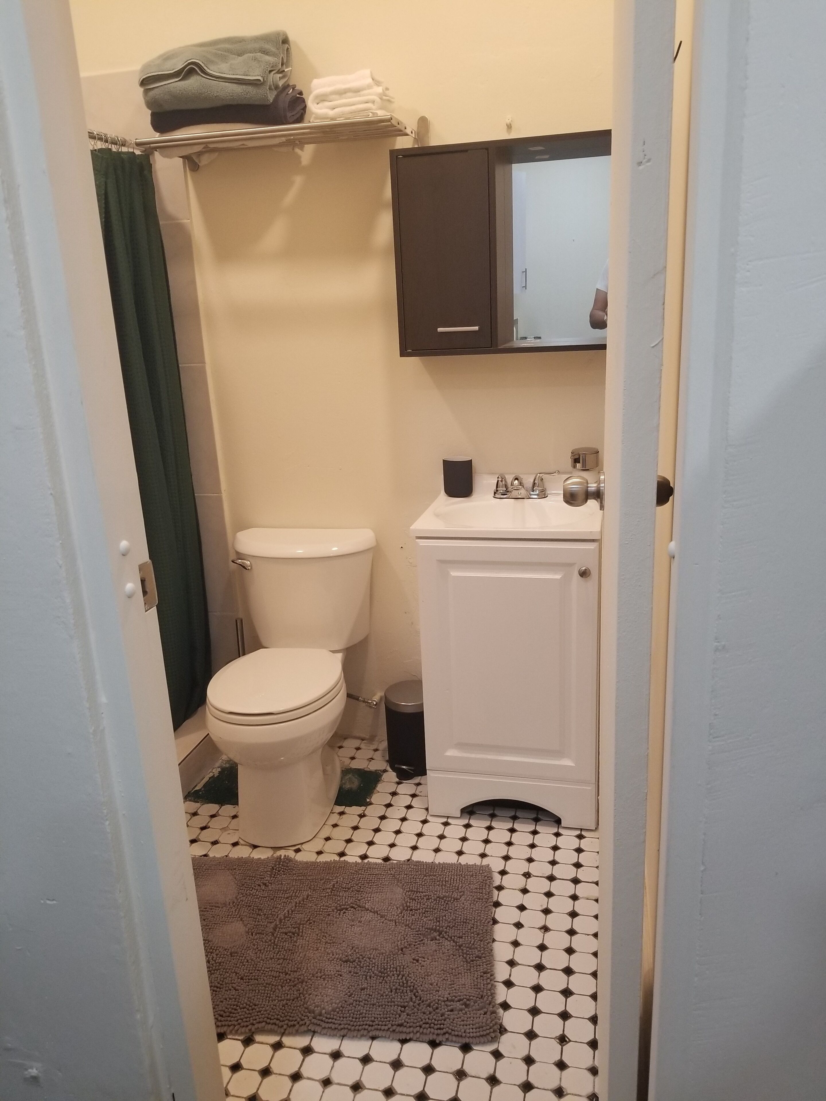 Un baño con inodoro, lavamanos, espejo y perchero para toallas.