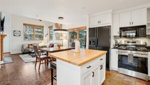 Una cucina moderna con mobili bianchi, un'isola in legno, elettrodomestici in acciaio inossidabile e un'area pranzo con divano e tavolo.