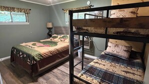 Ein Zimmer mit zwei Etagenbetten, einem Deckenventilator, einem Fenster mit Vorhang und einer Nachttischlampe.