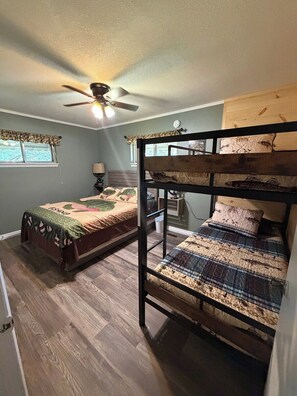 A room with two bunk beds, a ceiling fan, a window with a curtain, and a bedside lamp.