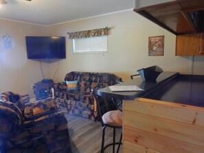 A compact living space with a television, a patterned sofa, a bar area, and a wooden cabinet.