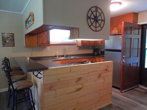 Una cocina con muebles de madera, una isla central con taburetes de bar, un lavamanos y un refrigerador.