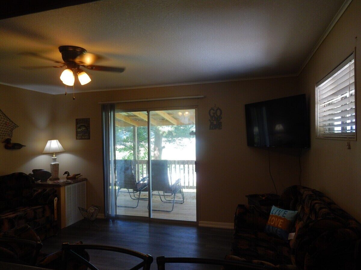 A living room with a ceiling fan, a television, a sofa, and a sliding glass door leading to an outdoor patio area.